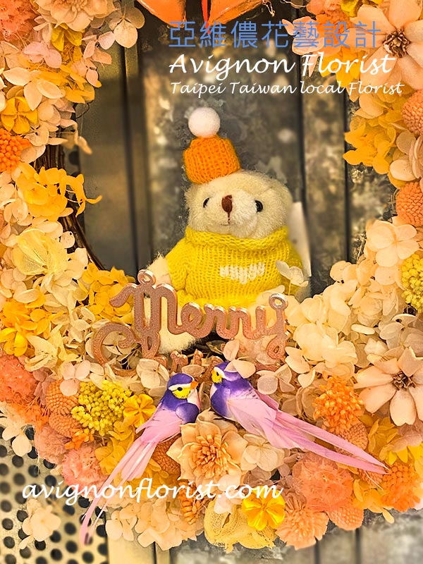 Close-up of a tiny bear in a sweater and winter hat nestled inside the preserved flower wreath.